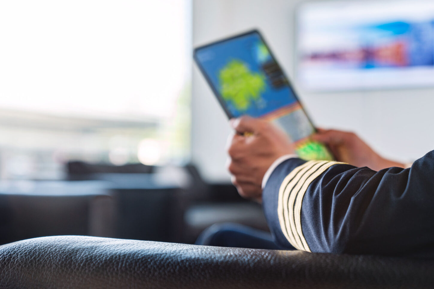 close up on the arm of a pilot in his uniform, sitting in a lounge and looking at a map on a tablet