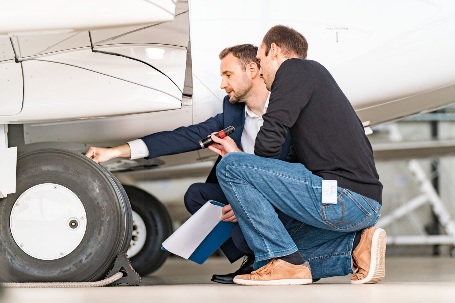 two aircraft specialists doing safety checks on the wheels of a parked aircraft